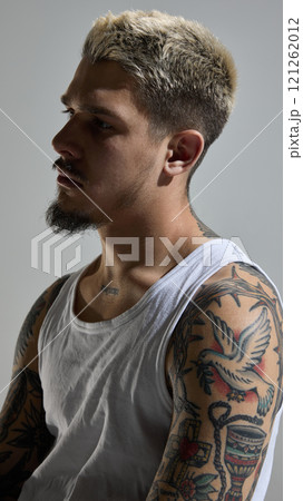 Portrait of handsome young man with blonde hair, beard and tattoos body, wearing tank top and posing with thoughtful expression 121262012