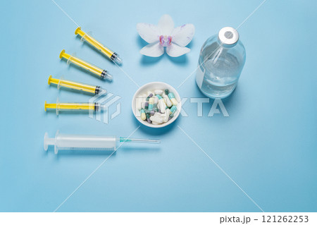 Bowl with capsules, a glass bottle with liquid medicine, big and small plastic syringes on the blue background. Bowl with capsules, a glass bottle with liquid medicine, big and small plastic syringes on the blue background. 121262253