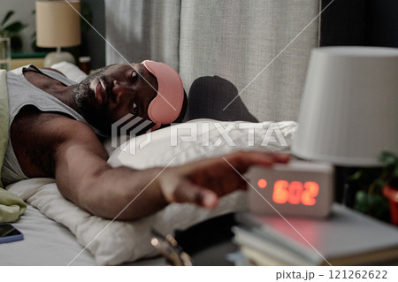 African American man with rose sleep mask on forehead stopping alarm in morning 121262622