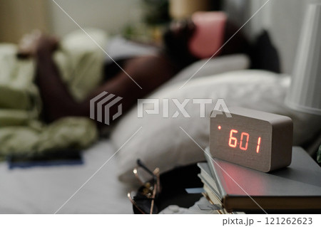 High angle shot of modern alarm clock on night stand next to bed with sleepy man High angle shot of modern alarm clock on night stand next to bed with sleepy man 121262623