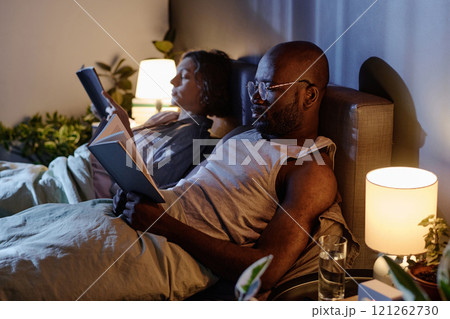 Medium close up of biracial couple lying in bed with books in hands reading stories Medium close up of biracial couple lying in bed with books in hands reading stories 121262730