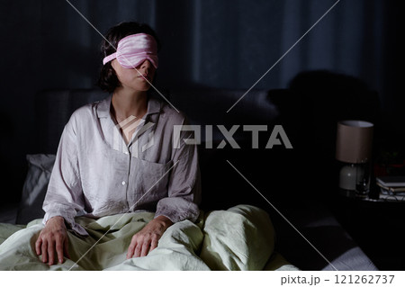 Woman with sleep mask rising from bed during late night at home Woman with sleep mask rising from bed during late night at home 121262737