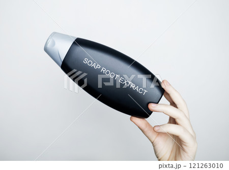 Female hands hold a bottle of shampoo, on which the ingredient is written - soap root extract. The concept of safe composition of organic shampoos Female hands hold a bottle of shampoo, on which the ingredient is written - soap root extract. The concept of safe composition of organic shampoos 121263010