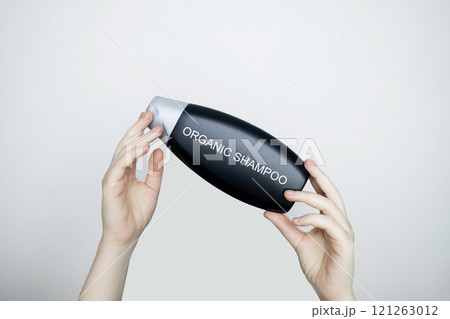 Female hands holding a bottle with the words - organic shampoo. Concept of safe composition and ingredients of environmentally friendly cosmetics and detergents 121263012