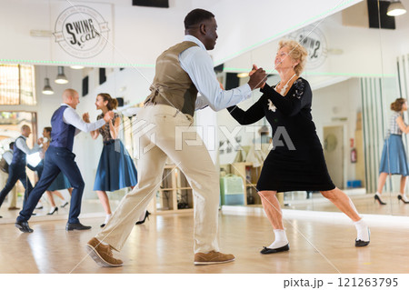 Woman pensioner with african man practising charleston Woman pensioner with african man practising charleston 121263795
