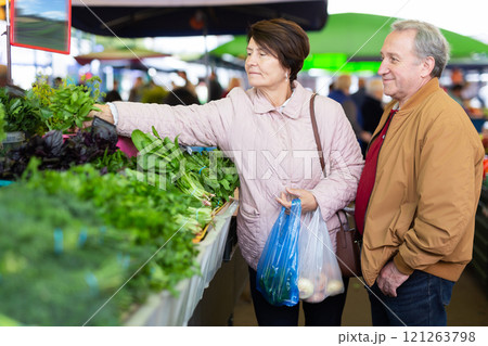 Positive elderly male and female choosing basil while buying greenery at local grocery market 121263798