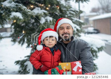 Father and his son are holding Christmas presents in front of a decorated Christmas tree while it snows 121265446