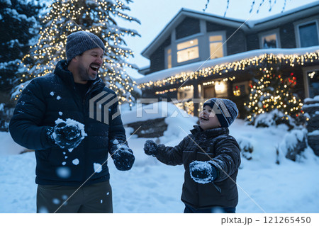 Father and his son are having fun playing snowballs together in the evening in front of their house decorated with Christmas lights 121265450