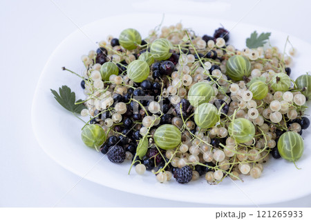 Fresh currants: black currants, white currants, blackberry and gooseberry. Mix of the berry on the white plate 121265933