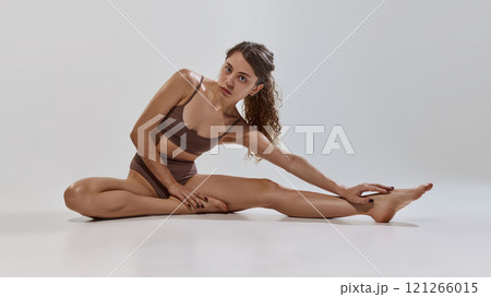 Fitness model stretches elegantly, combining grace, flexibility, and physical strength to highlight movement against grey studio background. Fitness model stretches elegantly, combining grace, flexibility, and physical strength to highlight movement against grey studio background. 121266015
