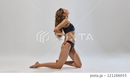 Confident, young, slender woman posing in black underwear and showing her fit, slim body against grey studio background. 121266055