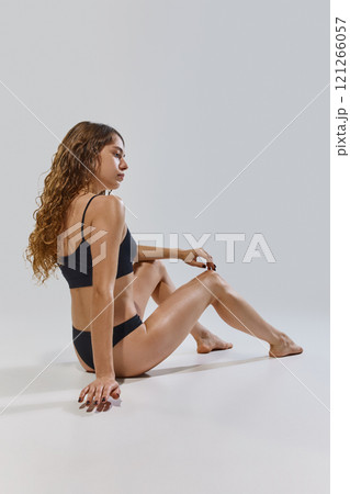 Rear view of young attractive woman posing confident sitting on floor against grey studio background. Wellness. Rear view of young attractive woman posing confident sitting on floor against grey studio background. Wellness. 121266057
