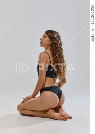 Rear view photo of young attractive, slender woman posing in black underwear against grey studio background. Rear view photo of young attractive, slender woman posing in black underwear against grey studio background. 121266059