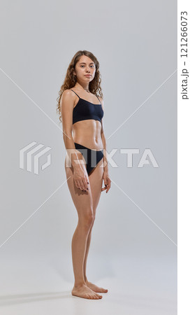 Young attractive woman posing in black lingerie showing her slim figure against grey studio background. Fitness. 121266073