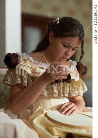 Vertical portrait of young girl concentrating on needlework while sitting in ornate chair in vintage interior, copy space Vertical portrait of young girl concentrating on needlework while sitting in ornate chair in vintage interior, copy space 121266541