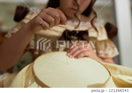 Close up of young lady guiding thread through fabric doing intricate embroidery in vintage setting, copy space 121266543