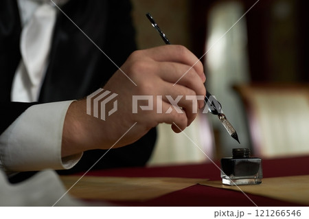 Side view close up of male hand dipping fountain pen in ink while writing letters in classic traditional setting, copy space Side view close up of male hand dipping fountain pen in ink while writing letters in classic traditional setting, copy space 121266546