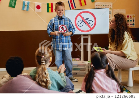 Full length shot of smiling young boy holding No walking sign while presenting road safety rules to kids in school classroom copy space Full length shot of smiling young boy holding No walking sign while presenting road safety rules to kids in school classroom copy space 121266695