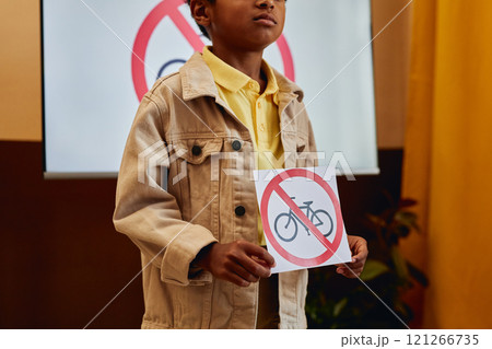 Close up of young African American boy holding No bicycles sign while giving presentation on road safety in primary school classroom copy space 121266735