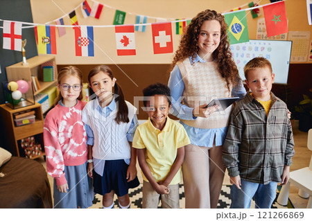 High angle view of smiling young woman as female teacher with group of children looking at camera standing in colorful primary school classroom High angle view of smiling young woman as female teacher with group of children looking at camera standing in colorful primary school classroom 121266869