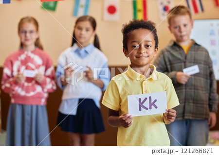 Waist up portrait of African American boy holding letter card and looking at camera with group of children learning English in background Waist up portrait of African American boy holding letter card and looking at camera with group of children learning English in background 121266871