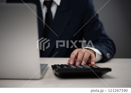 Businessman using a calculator alongside a laptop for financial analysis and budgeting tasks. Represents accounting, financial planning, and data analysis in a corporate setting. Businessman using a calculator alongside a laptop for financial analysis and budgeting tasks. Represents accounting, financial planning, and data analysis in a corporate setting. 121267390