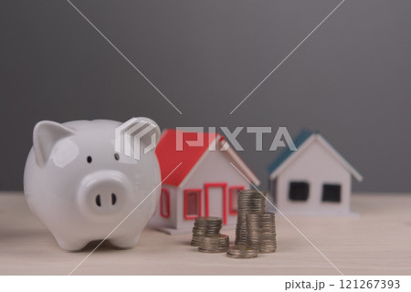Piggy bank with coin stacks and miniature houses representing home savings 121267393