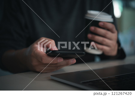 Close-up of person using smartphone while holding coffee cup at desk Close-up of person using smartphone while holding coffee cup at desk 121267420