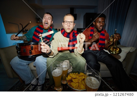 Fisheye front view of excited sports fans cheering and screaming sitting on couch together and wearing matching team scarves, shot with flash 121267480