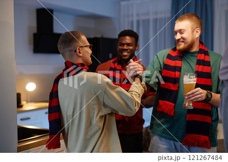Group of three male sports fans shaking hands and drinking beer while enjoying after game party at home and celebrating win 121267484