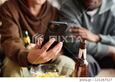 Close up of male hand holding smartphone with three friends looking at screen and drinking beer, copy space Close up of male hand holding smartphone with three friends looking at screen and drinking beer, copy space 121267527