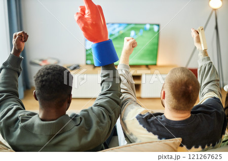 Back view of excited sports fans watching football match on TV at home sitting on couch and raising hands celebrating victory, copy space Back view of excited sports fans watching football match on TV at home sitting on couch and raising hands celebrating victory, copy space 121267625
