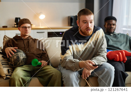 Front view portrait of devastated sports fans watching game together at home sitting on couch and holding TV remote 121267641