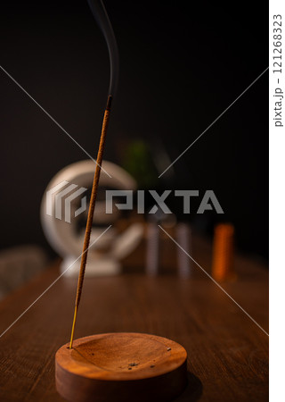incense stick smokes on a wooden stand on a dark background. Aromatherapy, Smoke while burning incense. smoke for prayers and meditation. prayer to buddha. incense for relaxation and yoga incense stick smokes on a wooden stand on a dark background. Aromatherapy, Smoke while burning incense. smoke for prayers and meditation. prayer to buddha. incense for relaxation and yoga 121268323