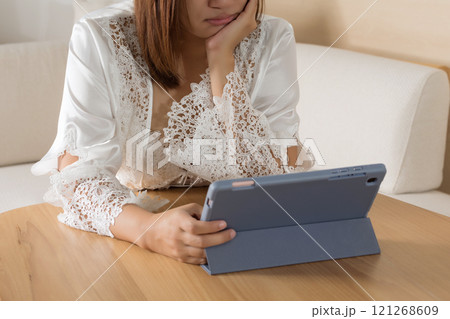 Woman in white silk sleepwear reads tablet at night. 121268609