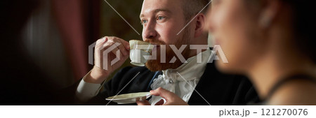 Header style portrait of young gentleman sipping tea delicately from porcelain teacup in classic setting 121270076
