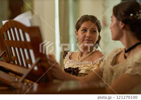 Portrait of smiling young girl wearing vintage dress playing piano with elder sister in vintage classic setting, copy space Portrait of smiling young girl wearing vintage dress playing piano with elder sister in vintage classic setting, copy space 121270100
