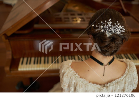 Back view closeup of classic young lady with pearl hair accessory playing grand piano in elegant interior, copy space Back view closeup of classic young lady with pearl hair accessory playing grand piano in elegant interior, copy space 121270106