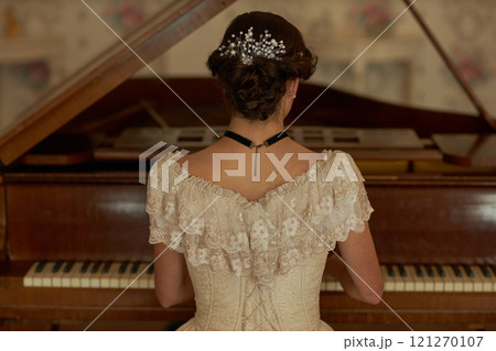 Back view of classic young lady wearing lace dress with pearls in hair playing grand piano in elegant interior, copy space Back view of classic young lady wearing lace dress with pearls in hair playing grand piano in elegant interior, copy space 121270107
