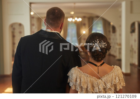Back view of lady and gentleman wearing formal attire walking into ballroom in softly lit classic interior, copy space 121270109