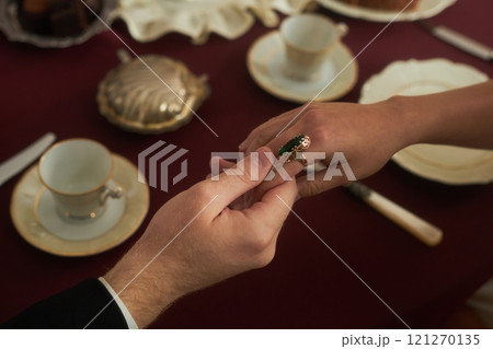 Top view closeup of unrecognizable gentleman holding young ladys hand gently over richly vintage red table at tea service, copy space 121270135