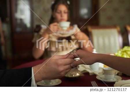Side view closeup of classic lady and gentleman holding hands gently over richly set table with blurred background, copy space 121270137