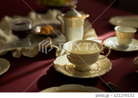 Close up of elegant porcelain tea cup with saucer on crimson tablecloth illuminated by natural light, copy space 121270152