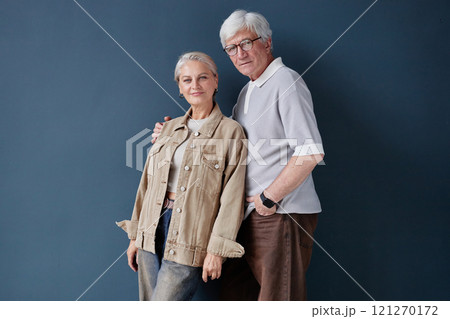 Minimal studio portrait of senior couple posing together against blue background and looking at camera lit by natural soft light Minimal studio portrait of senior couple posing together against blue background and looking at camera lit by natural soft light 121270172