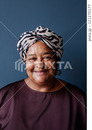 Vertical front view portrait of senior African American woman wearing headscarf and looking at camera with smile on blue background in studio 121270177