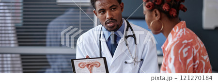 Cropped shot of male gynecologist wearing lab coat and holding tablet displaying female reproductive system diagram while talking to African American young woman 121270184