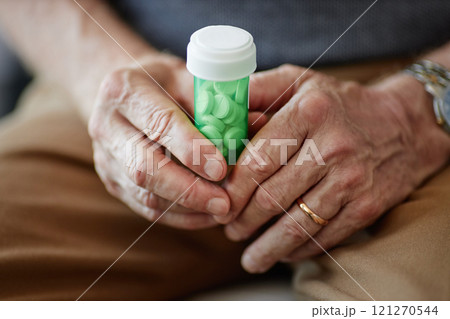 Close up of elderly man holding green prescription pill bottle in hands suffering from chronic illness, copy space Close up of elderly man holding green prescription pill bottle in hands suffering from chronic illness, copy space 121270544