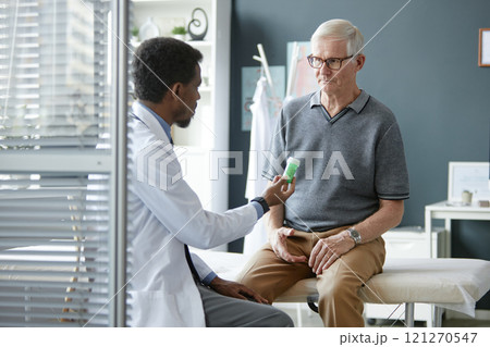 Back view of doctor holding green prescription bottle while discussing medication and treatment plan with senior man during consultation in clinic Back view of doctor holding green prescription bottle while discussing medication and treatment plan with senior man during consultation in clinic 121270547