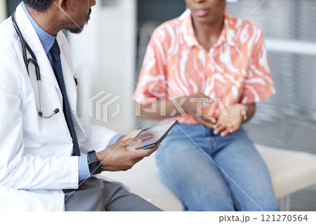 Side view of doctor wearing lab coat listening attentively to patient with woman gesturing in blurred background during consultation in clinic, copy space Side view of doctor wearing lab coat listening attentively to patient with woman gesturing in blurred background during consultation in clinic, copy space 121270564