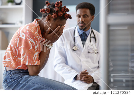 Side view of African American woman crying in doctors office and covering face with hands after getting shocking news during consultation in clinic, copy space Side view of African American woman crying in doctors office and covering face with hands after getting shocking news during consultation in clinic, copy space 121270584